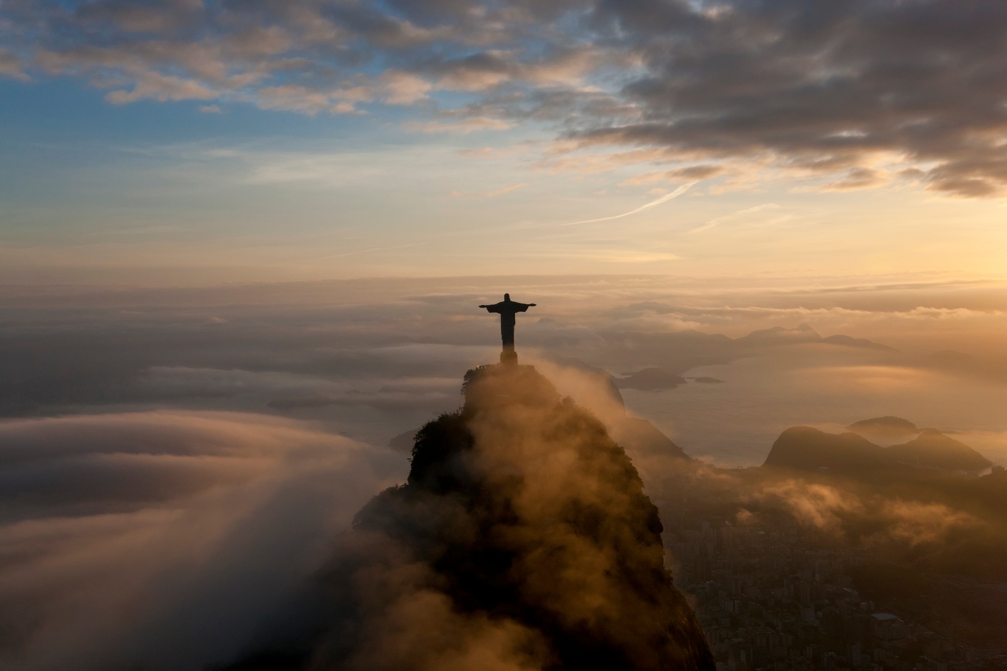 High angle view of colossal Christ Redeemer statue surrounded by clouds at dusk, Corcovado, Rio de